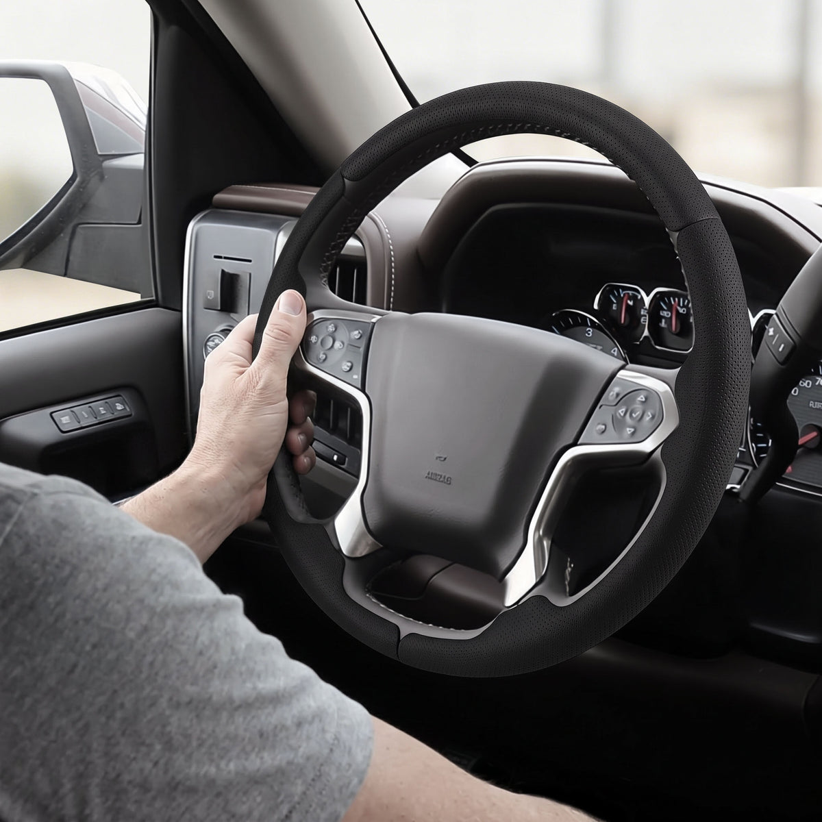Installed view of black perforated leather 3-piece steering wheel cover for Chevy Silverado 1500 2014-2018 & Silverado 2500/2500HD/3500/3500HD 2015-2019 with driver holding the wheel#color=black perforated leather