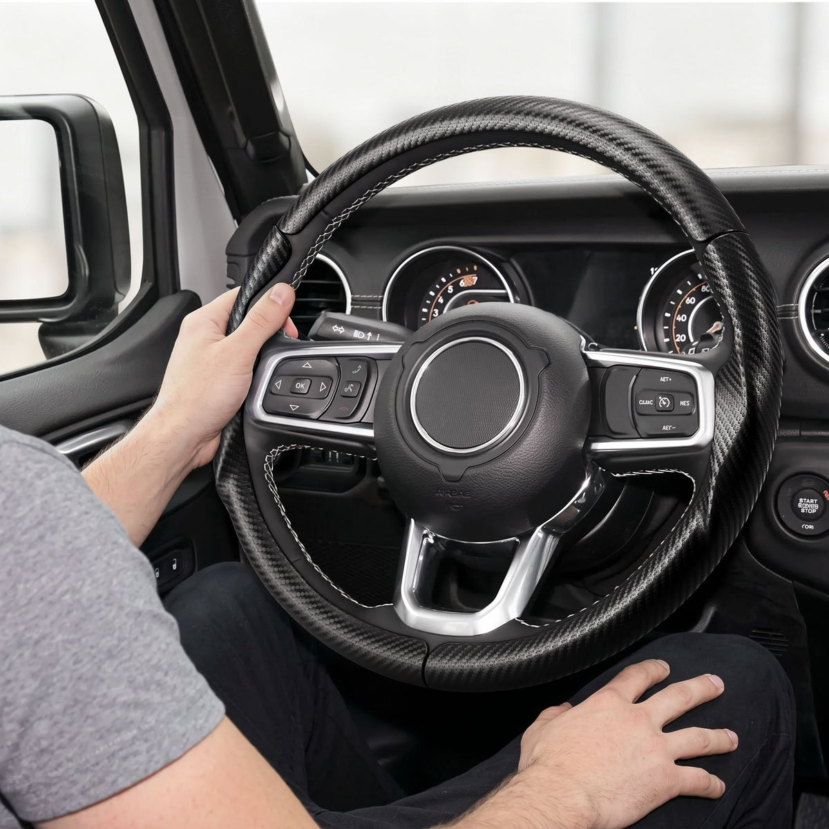 Installed view of matte black carbon-fiber-style 3-piece steering wheel cover for Jeep Wrangler 2018-2026 with driver holding the wheel#color=matte black