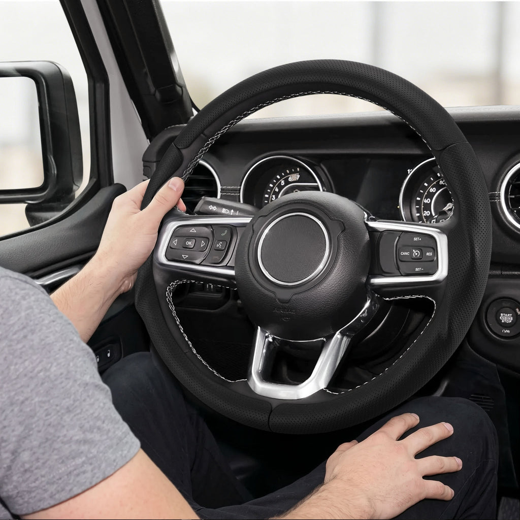 Installed view of black perforated leather 3-piece steering wheel cover for Jeep Wrangler 2018-2026 with driver holding the wheel#color=black perforated leather