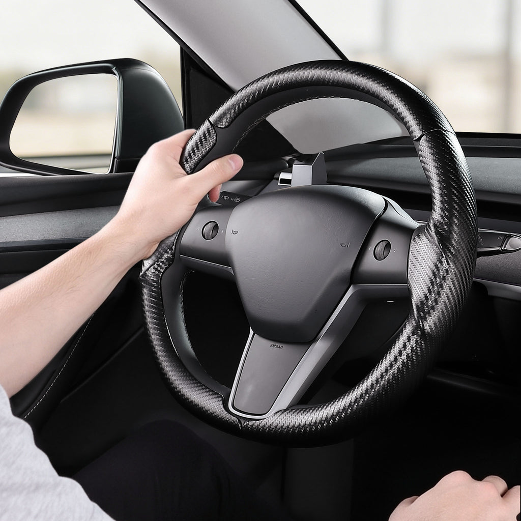 Installed view of matte black carbon-fiber-style 3-piece steering wheel cover for Tesla Model Y 2020-2024 with driver holding the wheel#Model=Model Y 2020-2024|color=matte black