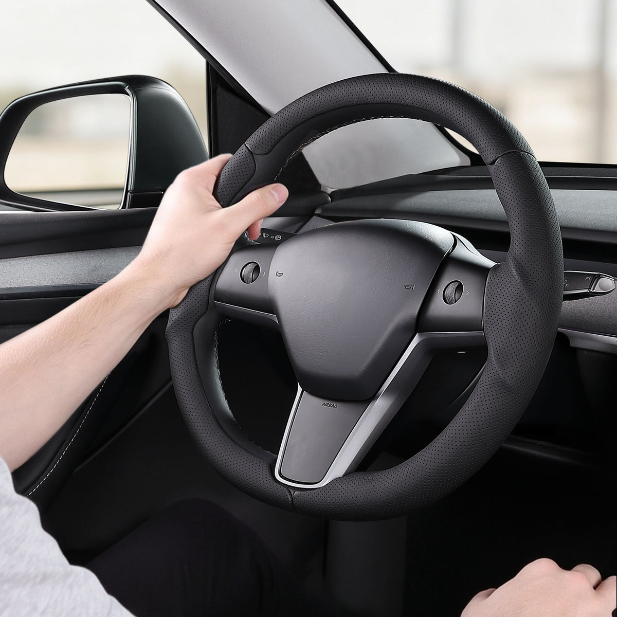 Installed view of black perforated leather 3-piece steering wheel cover for Tesla Model Y 2020-2024 with driver holding the wheel#Model=Model Y 2020-2024|color=black perforated leather