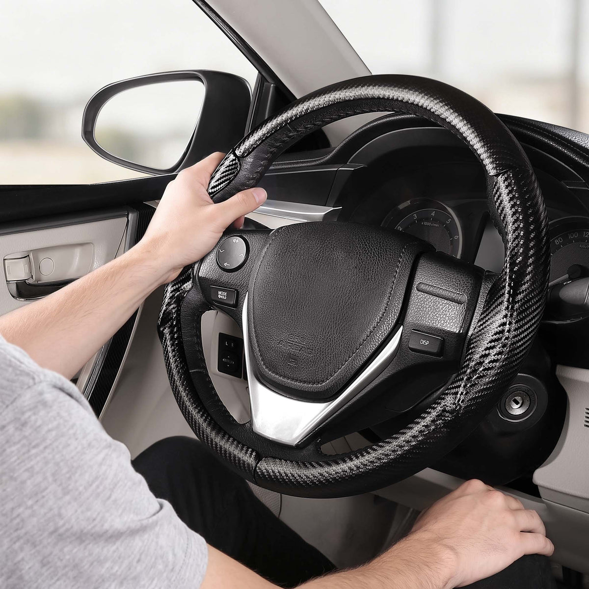 Installed view of matte black carbon-fiber-style 3-piece steering wheel cover for Toyota Camry 2015-2017 & Camry SE 2012-2014 with driver holding the wheel#color=matte black