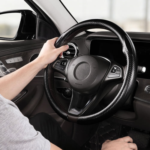 Installed view of matte black carbon-fiber-style steering wheel cover for 14.5-15 Inch Wheels with driver holding the wheel#color=matte black
